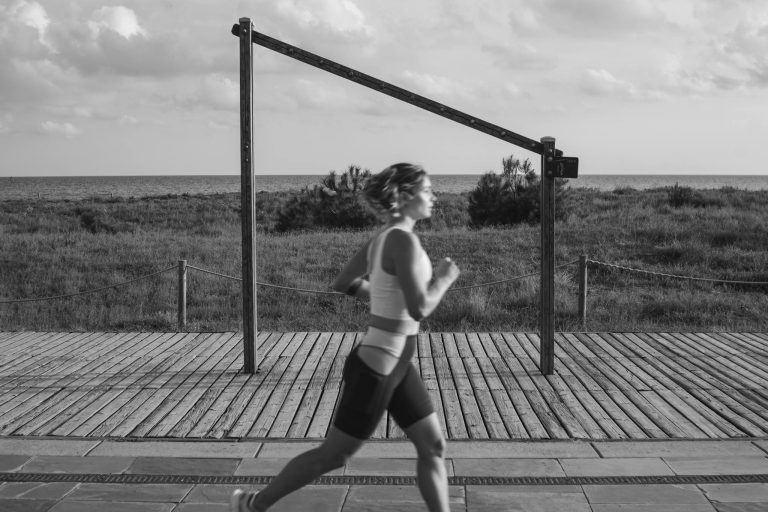 A woman jogs along a coastal boardwalk in Castelldefels, Spain, promoting fitness and outdoor exercise.
