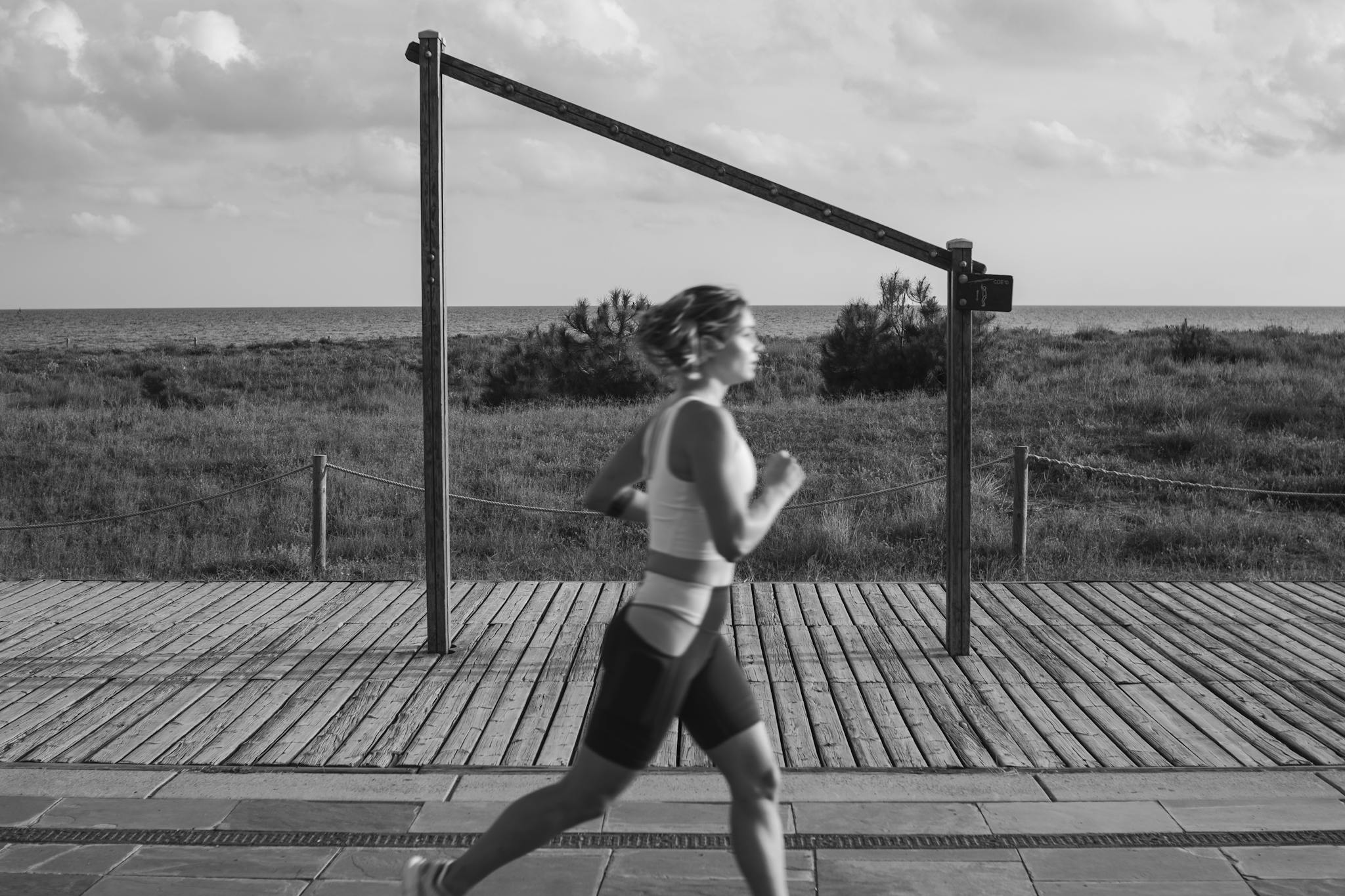 A woman jogs along a coastal boardwalk in Castelldefels, Spain, promoting fitness and outdoor exercise.