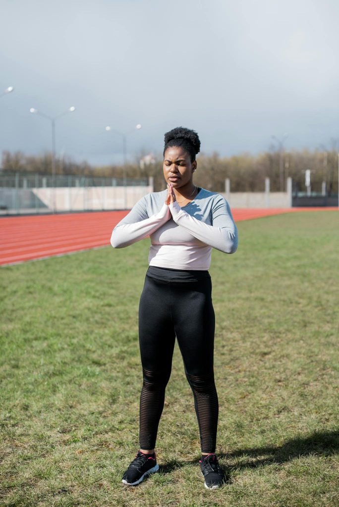 A woman practicing meditation outdoors on a sunny day near a running track.