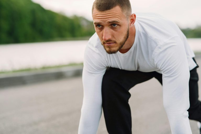 Athletic man in sportswear on a starting line, ready for a sprint workout outdoors.